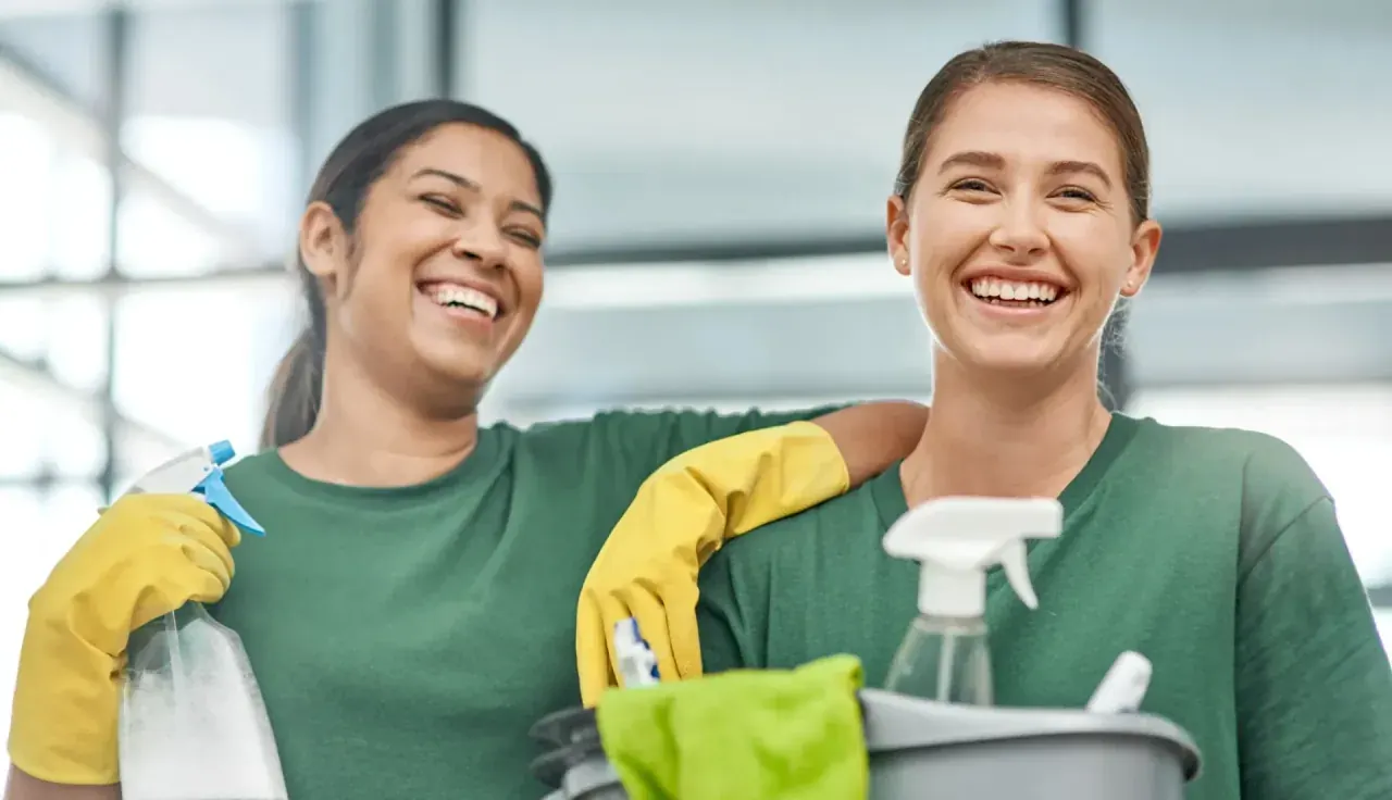 Two smiling CQD cleaners in green uniforms with commercial cleaning supplies